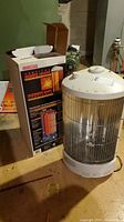 Celebrity Vertical Quartz Heater with original box showing front and side views, placed on a workbench.