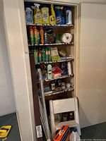 Photo of closet shelves filled with assorted cleaning supplies, paper towels, and household items.