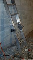 Full view of the convertible aluminum ladder extended in step ladder form against a concrete block wall, showing the rungs and red rubber feet.
