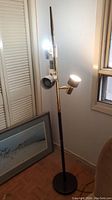 Full view of mid-century modern floor lamp with three lit adjustable lights and original tag visible on the pole, black circular base.