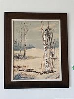 Frontal view of original painting in frame depicting birch trees and moody sky with lake in background.