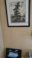 Framed print hanging on a wall, showing the pine tree artwork with part of the surrounding room visible.