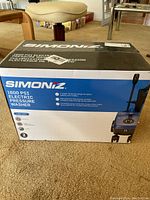 Front and top of the boxed Simoniz 1600 PSI electric pressure washer showing the product name and basic features.