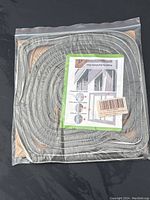 Photo of the coiled 16.5ft window sealing strip in clear plastic packaging, with instruction sheet visible.