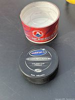 Photo showing black 2006 Calder Cup Finals official game puck alongside its original red metal container with AHL logos.