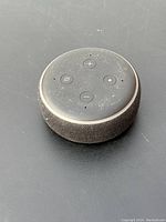Top view of Amazon Echo Dot round smart speaker showing four control buttons and some dust on surface