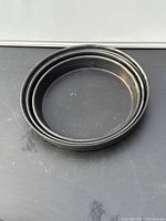Three nested round black metal cake baking pans stacked together, showing size variation and wear.