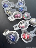 Lot of 9 colorful Hatchimals Colleggtibles figures in individual clear plastic capsules arranged on a dark surface showing variety of animals and creatures.