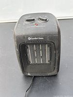 Front view of black Comfort Zone portable electric heater showing metal grill and control knobs on top.