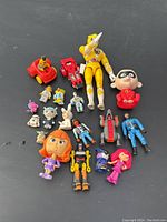 Overview of mixed figures including yellow Power Ranger, vehicles, collectible cartoon heads, and small plastic figures.