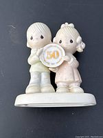 Full view of Precious Moments figurine showing boy and girl holding anniversary plaque on a flat base.