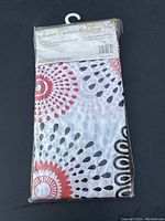 New packaged shower curtain and ring set with circular pattern design in red, black, and grey on white background.
