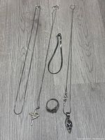 Five sterling silver jewelry pieces arranged on floor: three necklaces including two with charms, one ring, one bracelet.