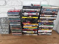 Full view of over 50 DVDs, 30+ CDs stacked separately, and a black decorative wooden sign with a motivational quote.