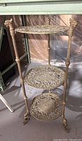 Full view of brass 3-tier plant stand showing dragon head details on the legs and ornate shelf patterns.
