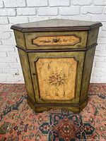 Front view of the flowered corner cabinet showing floral painted drawer and door in olive green and brown trim.