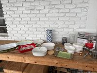 Overview of all kitchen items on wooden table showing Ninja box, CorningWare dishes, ceramic platters, and decor items