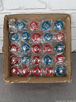 Top-down view of 30 red and blue M&M's yo-yos individually wrapped in clear plastic in a cardboard box, arranged in a grid