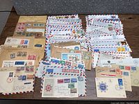 Wide view of a large assortment of old envelopes with stamps, laid out on a surface showing many air mail and brown paper envelopes.
