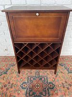 Front view of closed modern wine bar rack with drop-down door and wine bottle lattice storage below.