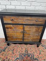 Front view of cabinet showing upper drawer and closed lower two doors with wood paneling and black painted frame.