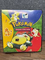 Front cover of Pokemon trading card binder with images of Pokemon characters Sandshrew, Meowth, Charmander and Snorlax