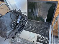 Full view of Toshiba laptop open with charger cable and black carrying bag next to it on a metal surface.