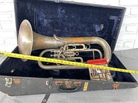 Vintage baritone horn inside its open black locking travel case with velvet interior, along with a Level One learning manual and measuring tape.