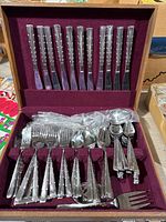 Full view of wooden box open displaying various knives, forks, and spoons arranged in slots lined with burgundy fabric.