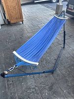 Full view of blue hammock stretched on blue metal stand on concrete floor.
