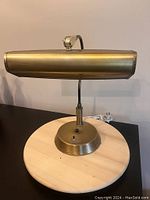 Front view of antique brass desk lamp with oval shade, round base, and curved neck on wooden surface.