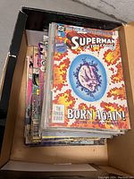 Box full of assorted Superman and other comics showing covers and edge of multiple comics