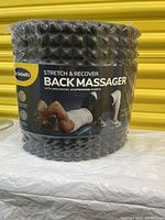 Front view of the black cylindrical back massager in shrink wrap with product branding and a person demonstrating its use.