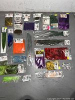 Top down view showing various fly tying material packets including feathers in multiple colors, synthetic fibers, spools of thread, dubbing also visible in original packaging