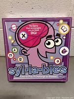 Front of the Syl-la-bles board game box showing playful cartoon head and colorful letters on purple background.