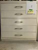 Front view of 5 drawer white dresser with brass handles, showing full piece and attached measurement notes.