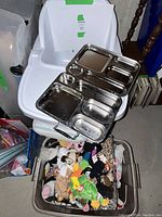 Convertible white high chair set with tray, placed next to a basket full of original Beanie Babies and assorted stuffed animals, with a stainless steel divided plate tray propped on top.