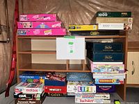 Photo showing the entire lot of boardgames and puzzles stacked on and around a wooden shelf. Several recognizable game titles and puzzles visible.