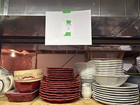Photo shows two stacked dishware sets: one red with 16 pieces and one white set with pitcher and creamer. Also includes vintage cane-patterned bowl and ceramic cookware dishes.