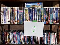 Two shelves filled with VHS tapes mostly Disney classics and DVDs, contained in cases with visible artwork and titles.