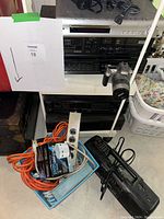 Stereo components stacked with cables, power strips, and a camera on the floor