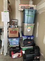 Tower of plastic storage totes, cardboard box and toolboxes stacked against unfinished wall