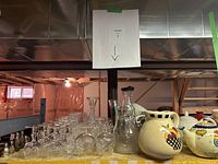 Photo shows a collection of vintage crystal glassware including wine, port, and whiskey glasses arranged on a table. Also visible are clear glass vases and various ceramic jugs with colorful patterns.