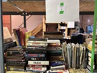Overview of lot showing stacks of vintage books, vintage maps in protective sleeves, and miscellaneous modern DVDs in plastic cases arranged on shelves