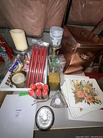Photo showing vintage copper-colored bread box, tapered candlesticks, boxed red taper candles, ivory candle, floral hot plate protectors, and decorative cards.