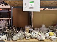 Photo of vintage silver candlesticks alongside assorted bone china cups and saucers with floral designs, clear glass bowls, and ceramic serving dishes.