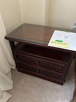 Front view of the vintage wooden end table showing glass top, open shelf, and drawers with keyhole hardware.