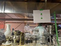 Various vintage glass houseware items including clear labeled jars, a green glass bottle, milk glass vase, metal candle holders, and metal bowls.