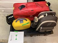 Photo of four items on top of a black travel trunk: a red leather suitcase, yellow compact case, brown picnic backpack, and a small black bag, showing the front and sides.