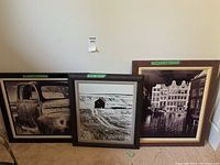 Three framed black and white photographic prints leaning against a wall, showing an old truck, a barn, and a canal town scene.